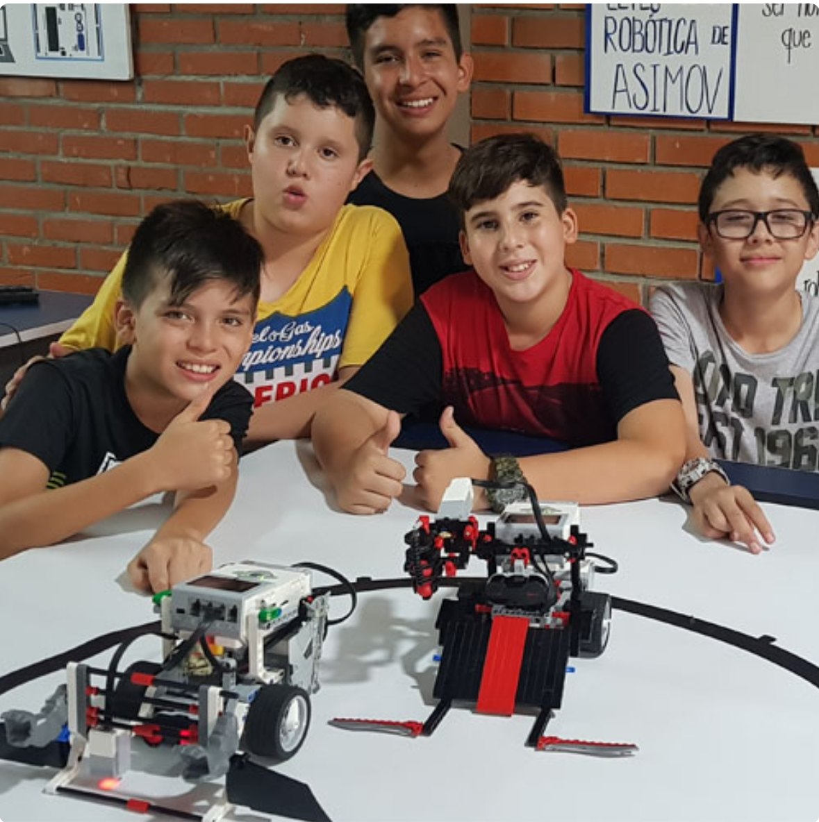 Cinco estudiantes del club con sus robots Lego EV3 en la arena de sumo, bajo un cartel con las leyes de la robótica de Asimov