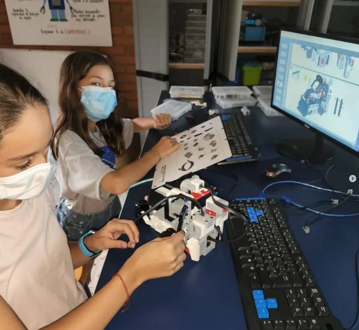 Dos estudiantes con tapabocas arman un robot Lego EV3 siguiendo las instrucciones en la pantalla del computador