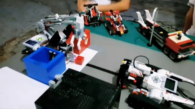 Varios robots Lego EV3 y NXT sobre una pista de pruebas, con un brazo y un camión de Lego Technic al fondo