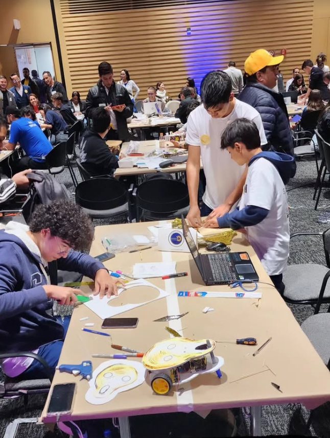 Los estudiantes construyen su robot sobre una mesa llena de cartón, herramientas y un portátil, durante la final
