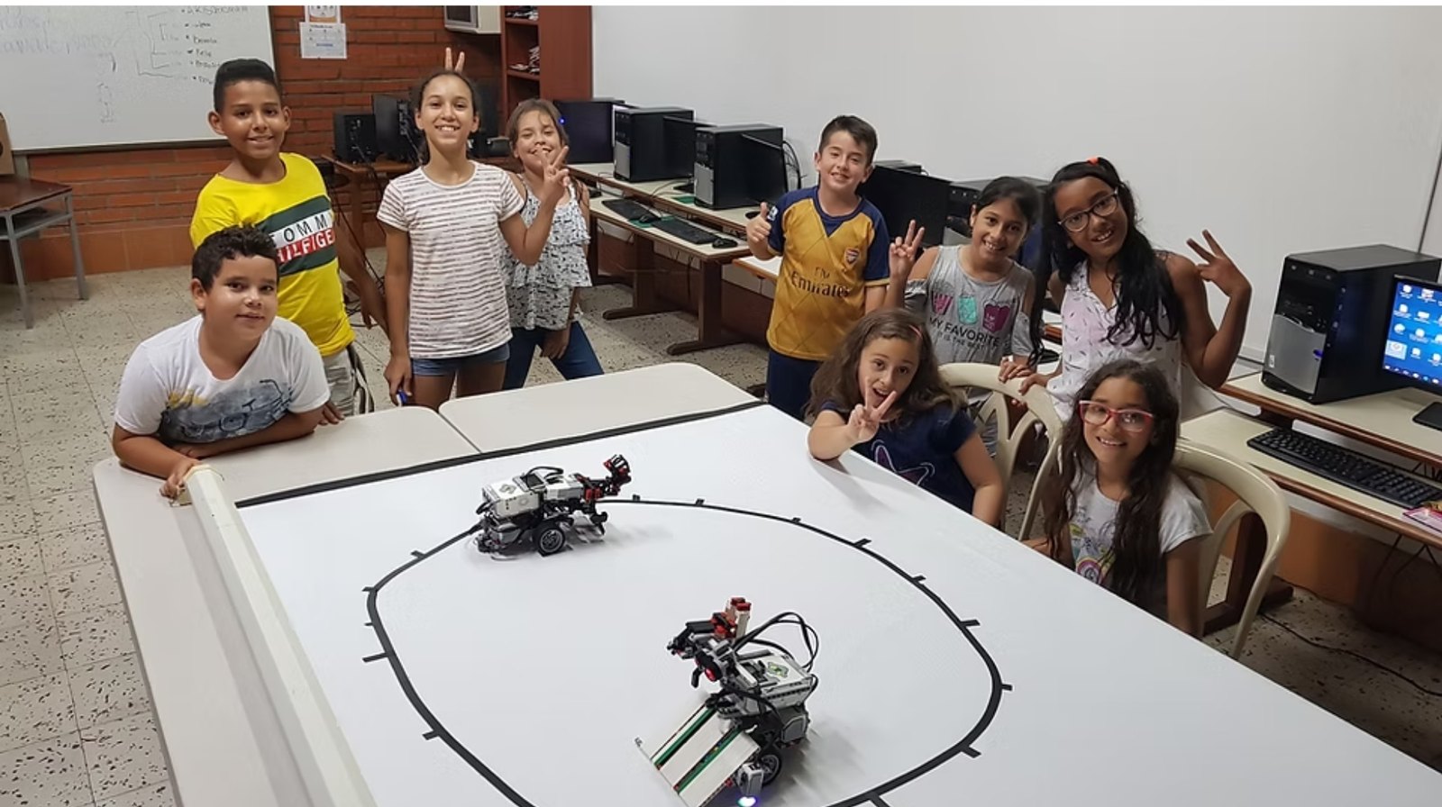 Estudiantes del club en el laboratorio, alrededor de la arena de sumo con dos robots