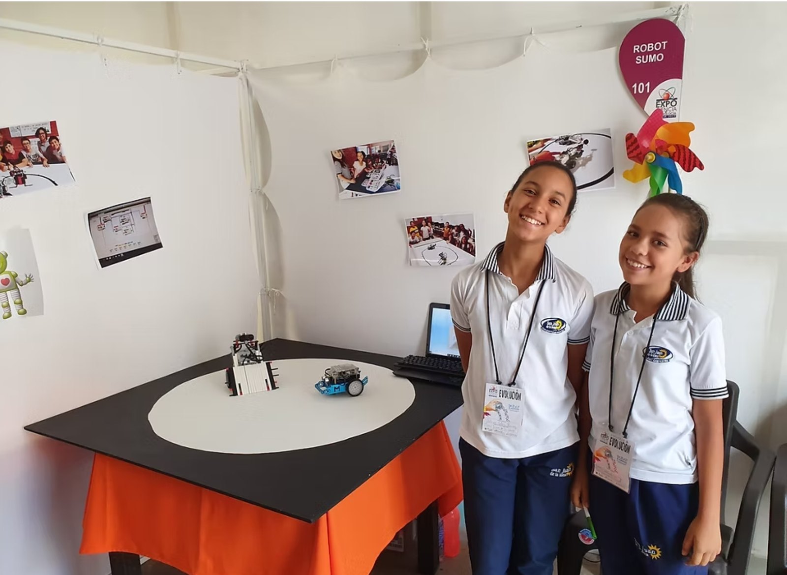 Dos estudiantes del club en su stand de Robot Sumo en una feria de ciencia, con la arena y los robots sobre la mesa