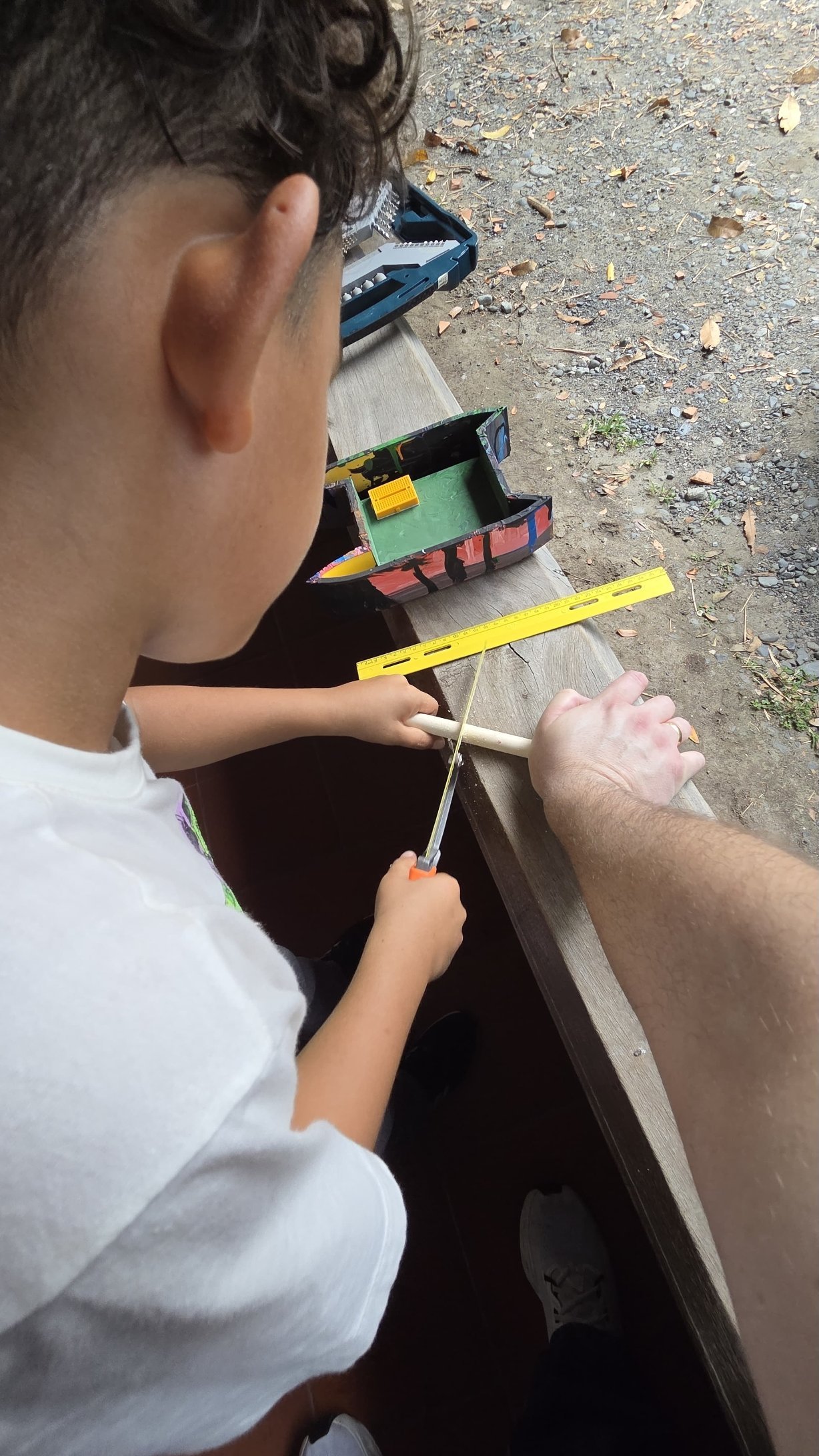 Un estudiante corta una varilla con una sierra de mano mientras el docente sujeta la pieza